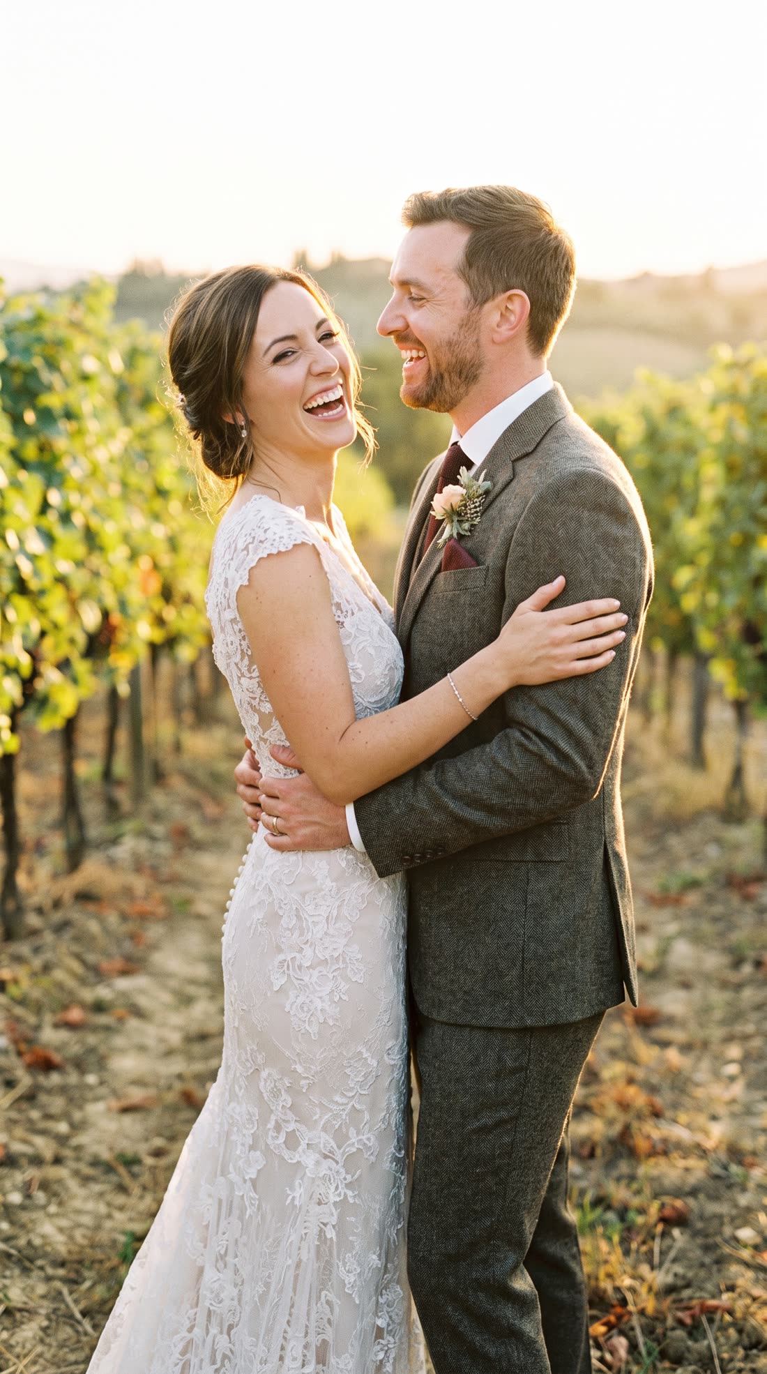 Casal recém-casado sorrindo abraçado em um vinhedo ao pôr do sol